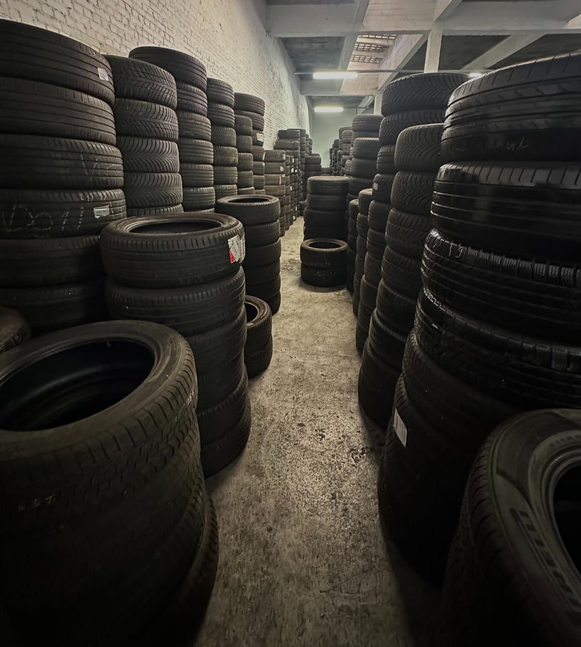 Gang tussen hoge stapels banden in het bandenmagazijn van WeFix Auto's.